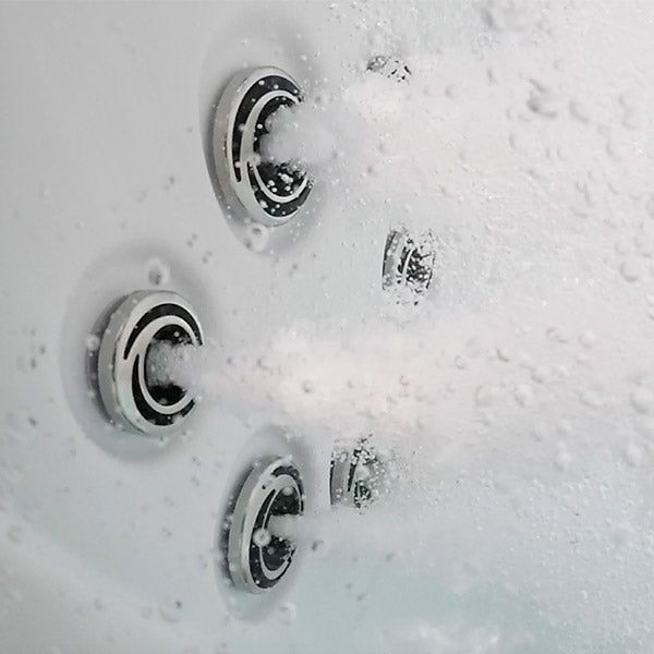 Close-up of a spa or hot tub jet system with multiple circular chrome nozzles spraying water and creating bubbles in a white tub interior.