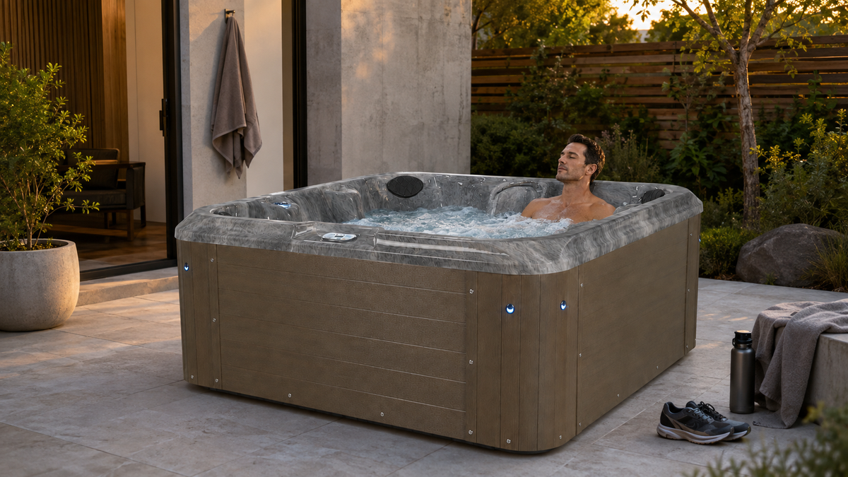 man in hot tub on patio with sneakers and workout clothing, trees house and plants in background