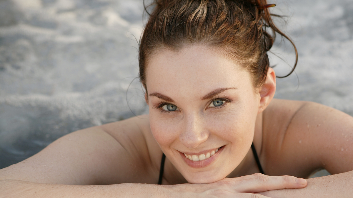 A smiling woman with wet hair leaning on her arms in a hot tub