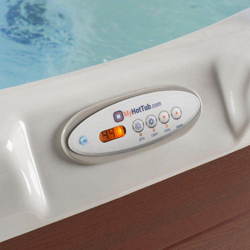 Close-up of a hot tub control panel mounted on a white hot tub edge, with blue pool water visible above and a brown wood-look surface below. The panel shows the MyHotTub logo.