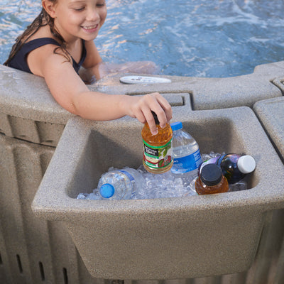 A child reaches into a built-in cooler tray of a hot tub filled with ice and bottled drinks, with water visible in the background.