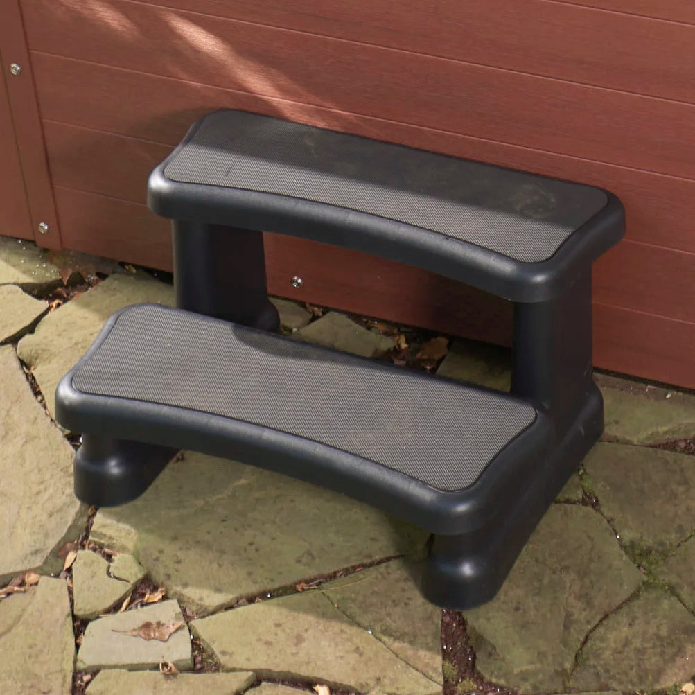 Two-step outdoor steps with textured non-slip grips, shown on a stone patio in front of a brown wooden hot tub.