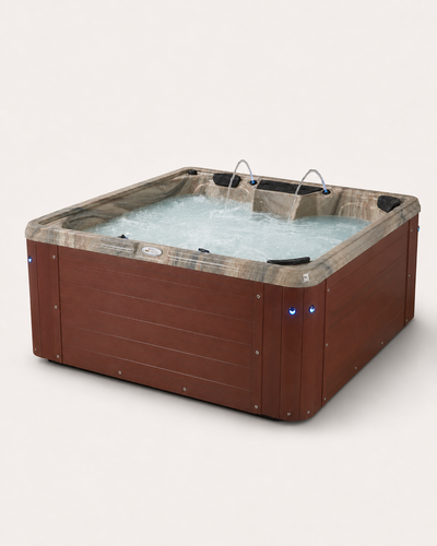A square hot tub with a brown wood-look exterior and a tan marbled shell filled with bubbling water. It features integrated metal nozzles and small blue LED light accents on the front corners, set against a plain light gray background. #cabinet_sonoma-redwood