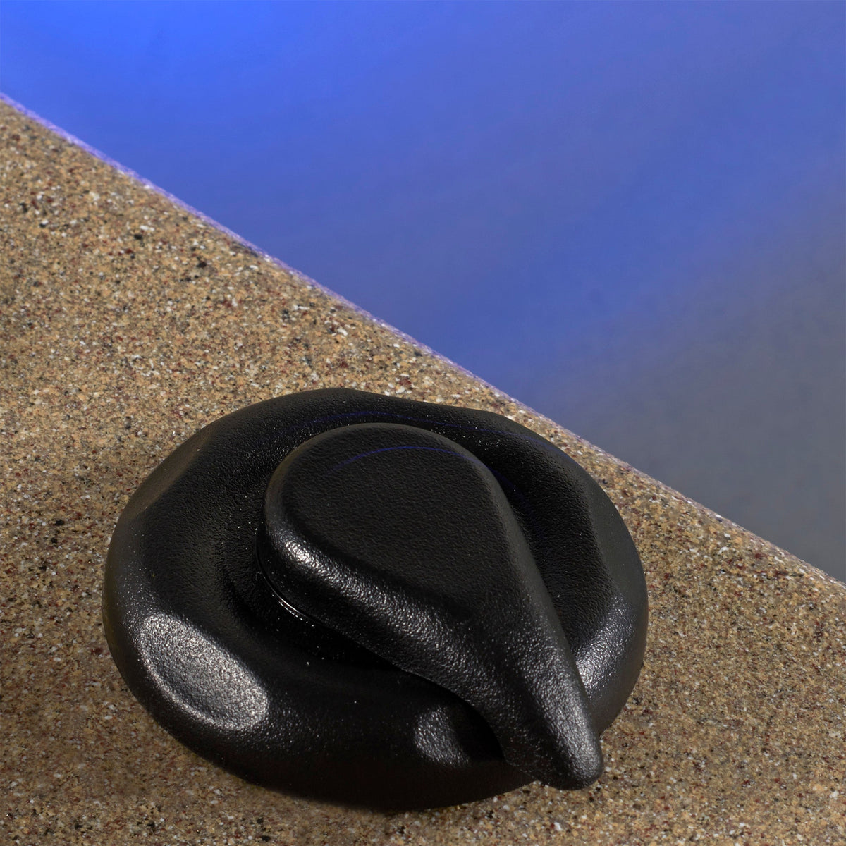 A close-up of a black plastic rotary dial control knob resting on a textured beige surface with a blue background.