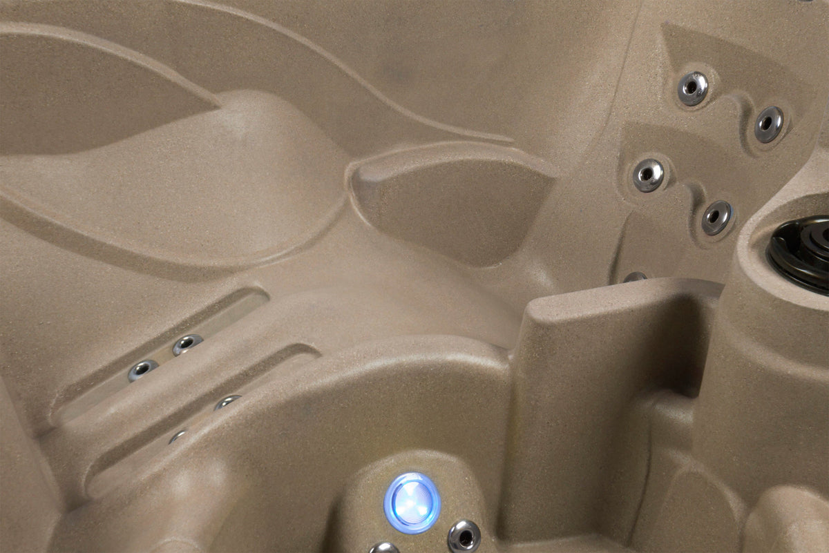 Close-up of a beige molded hot tub or spa interior with visible jets, lounger seat, and a blue illuminated control light.
