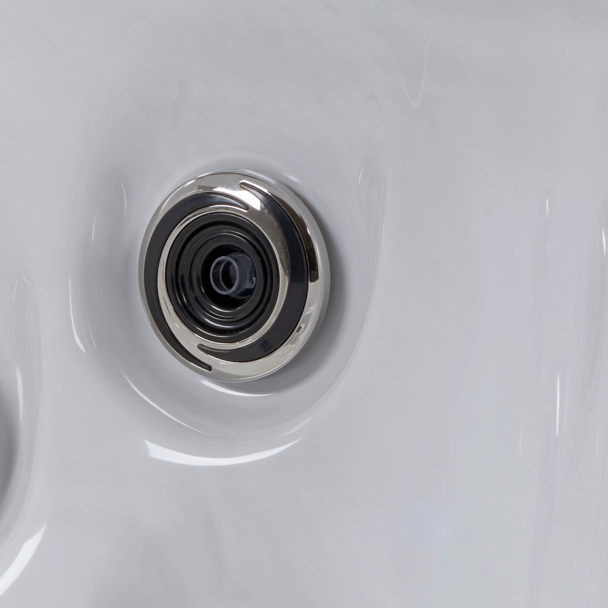 Close-up of a circular stainless steel spa jet on a white acrylic spa surface.