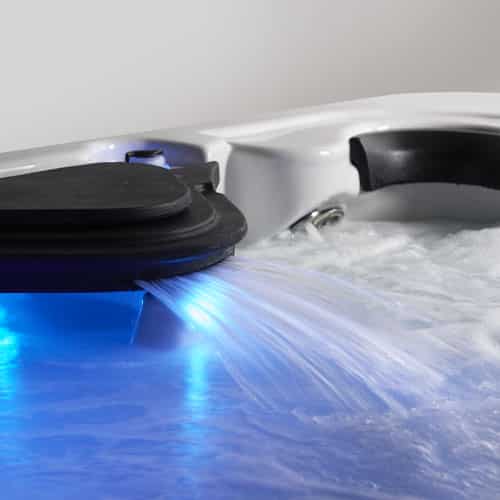 Hot tub with water flowing out of a waterfall illuminated by blue light.