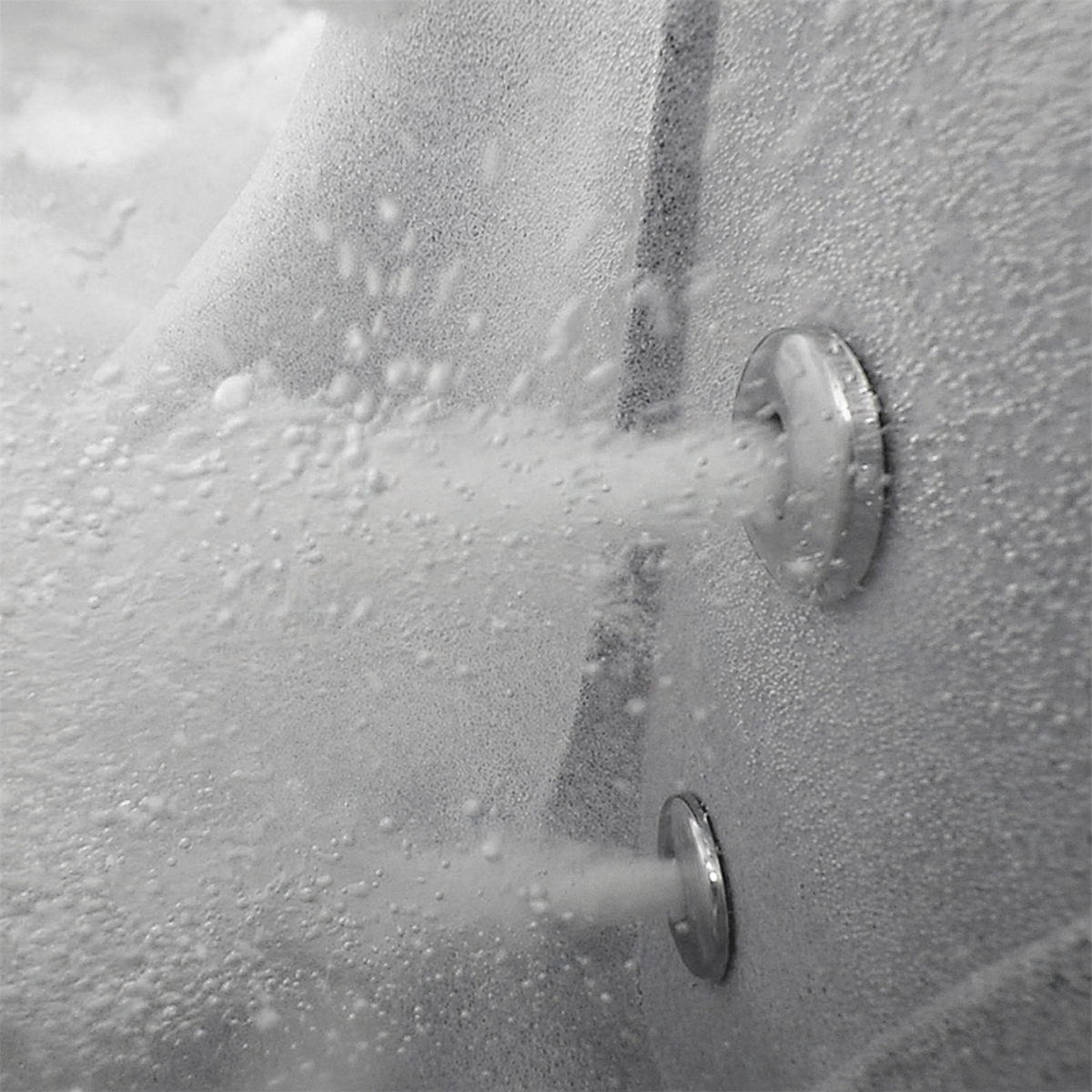 Close-up of a textured gray surface with two circular metal fixtures emitting fine white spray or mist.