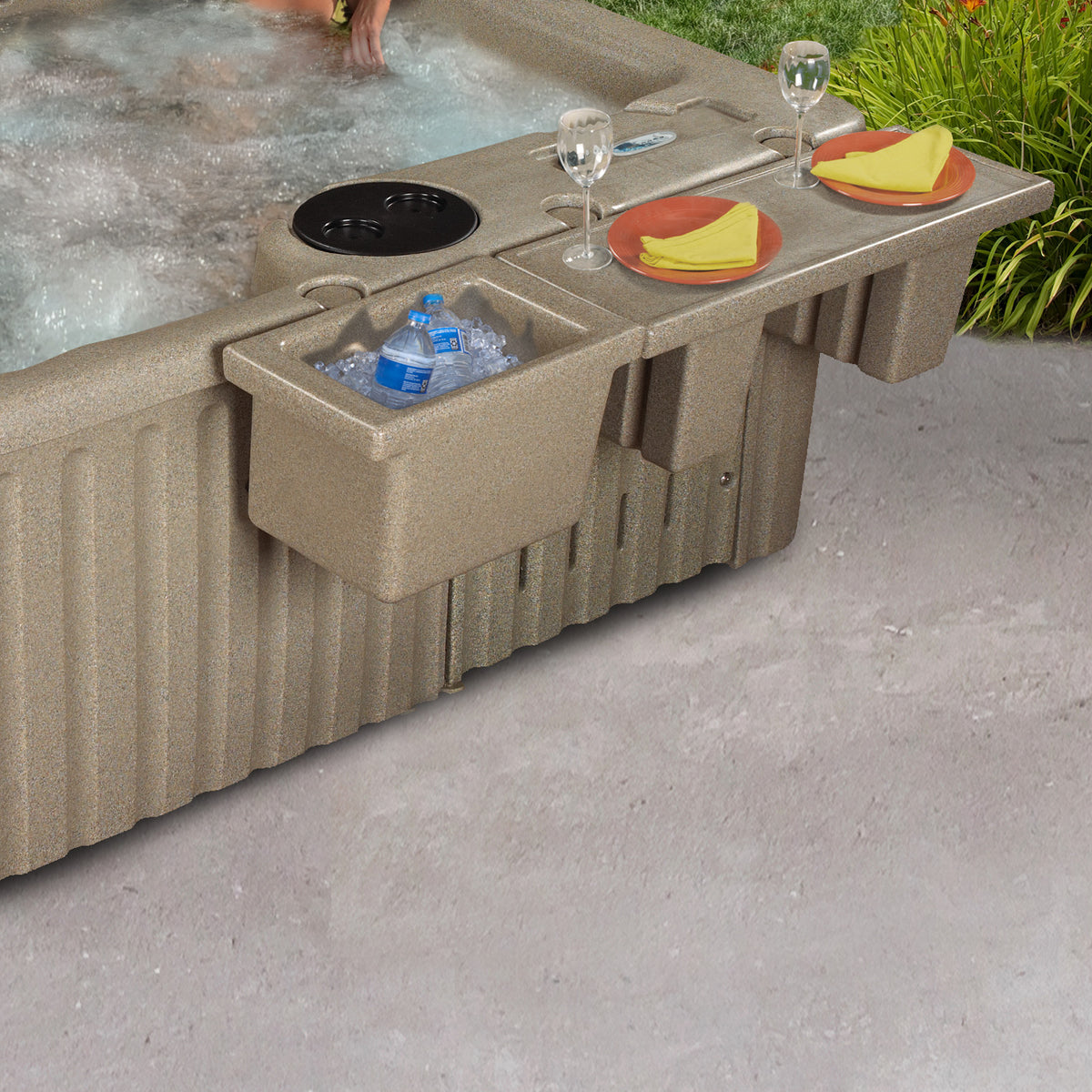 A beige hot tub with an integrated side bar and ice bucket, shown outdoors on a concrete patio with food and drink accessories placed on the bar.