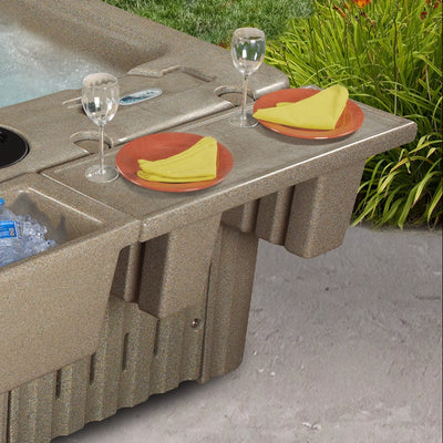 A beige hot tub with an integrated tray, shown outdoors on a concrete patio with food and drink accessories placed on the bar.
