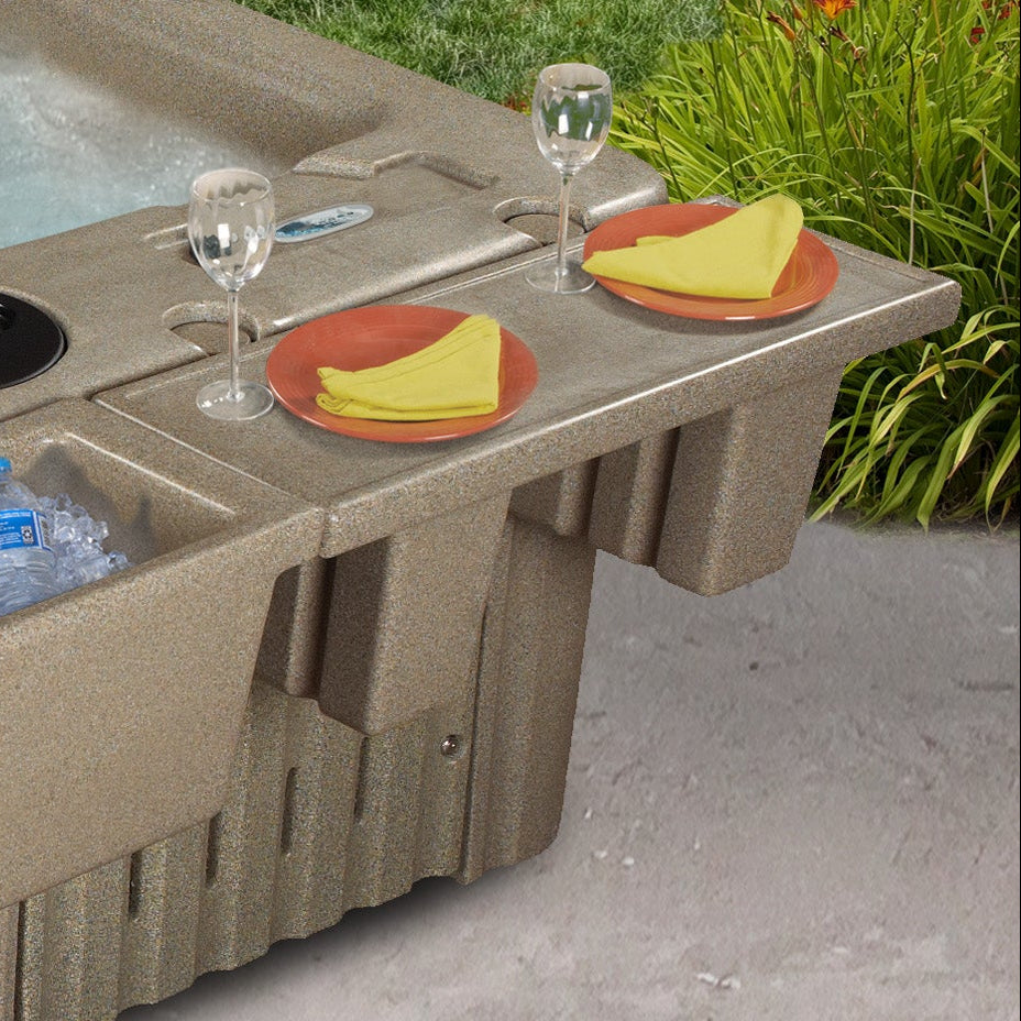 A beige hot tub with an integrated tray, shown outdoors on a concrete patio with food and drink accessories placed on the bar.