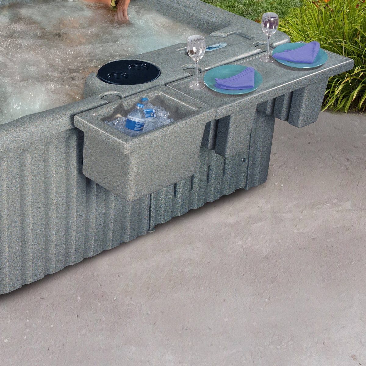A gray hot tub with an integrated side bar and ice bucket, shown outdoors on a concrete patio with food and drink accessories placed on the bar.