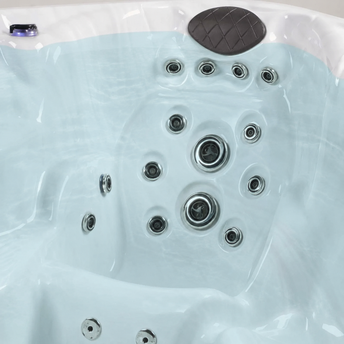 Close-up of a white hot tub interior with multiple silver jet nozzles, a dark gray textured backrest cushion, and a light aqua-tinted water surface.