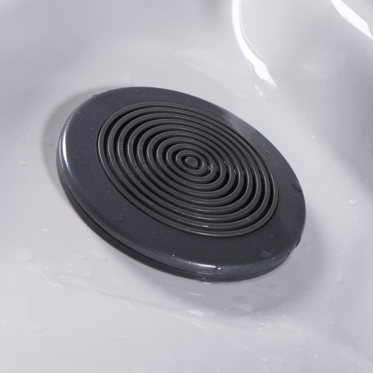 A round black speaker with concentric circular ridges, shown installed on a white acrylic spa surface.